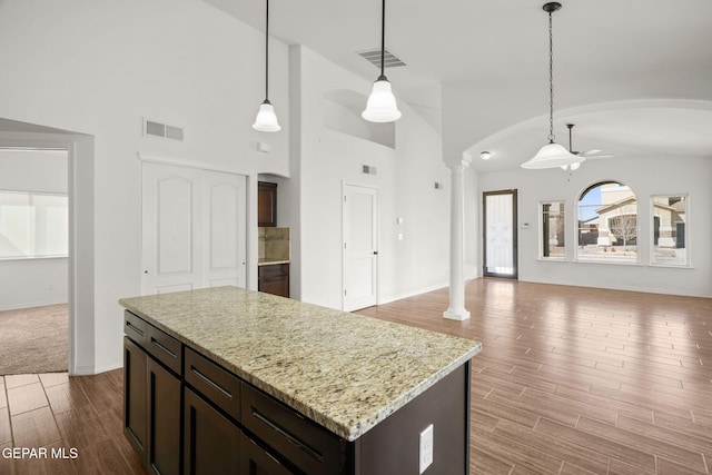 kitchen with decorative columns, pendant lighting, light stone counters, and light hardwood / wood-style floors