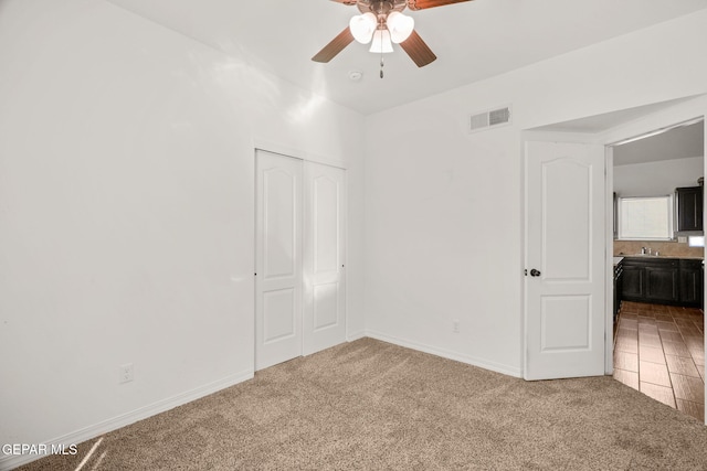 unfurnished bedroom featuring a closet, sink, carpet flooring, and ceiling fan