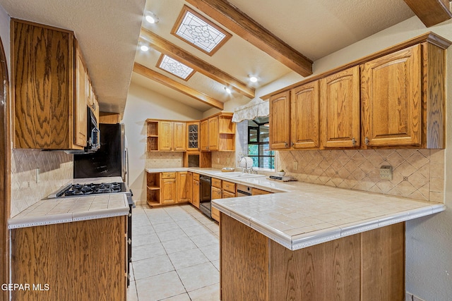 kitchen with tile countertops, kitchen peninsula, backsplash, and lofted ceiling with skylight