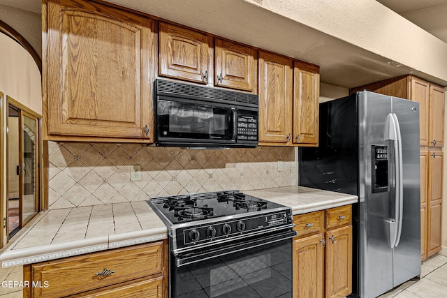 kitchen with black appliances, light tile patterned floors, backsplash, and tile countertops