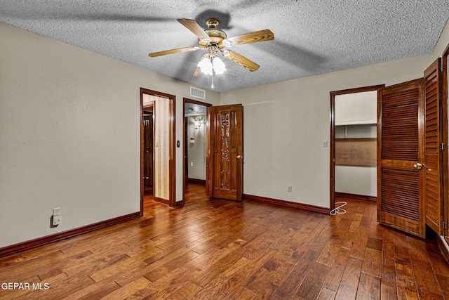 unfurnished bedroom with a walk in closet, dark hardwood / wood-style flooring, a textured ceiling, ceiling fan, and a closet