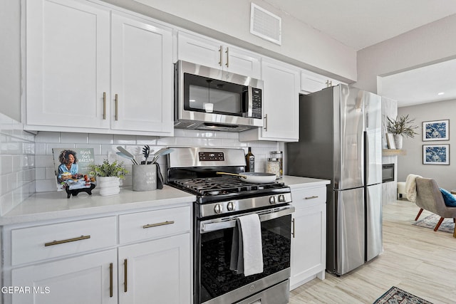 kitchen featuring stainless steel appliances, light hardwood / wood-style floors, white cabinetry, and backsplash