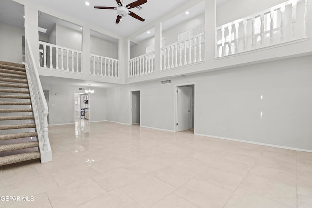 unfurnished living room with ceiling fan with notable chandelier, light tile patterned flooring, and a towering ceiling