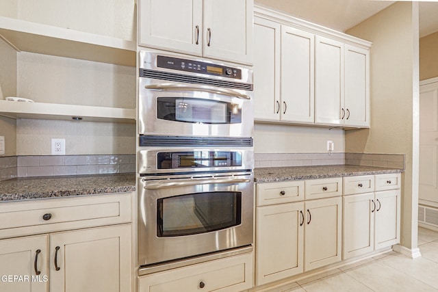 kitchen featuring dark stone countertops, light tile patterned floors, and double oven