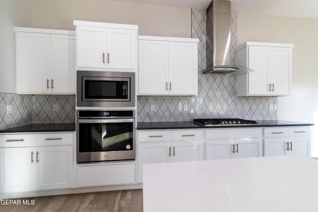 kitchen featuring tasteful backsplash, white cabinets, stainless steel appliances, and wall chimney range hood