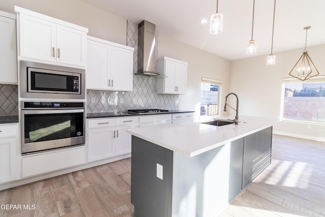 kitchen featuring pendant lighting, wall chimney exhaust hood, an island with sink, and appliances with stainless steel finishes