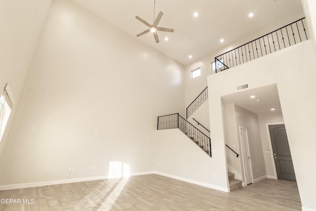 unfurnished living room with a high ceiling, light wood-type flooring, and ceiling fan