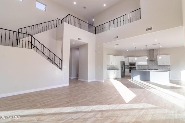 unfurnished living room with light hardwood / wood-style floors, sink, and a high ceiling