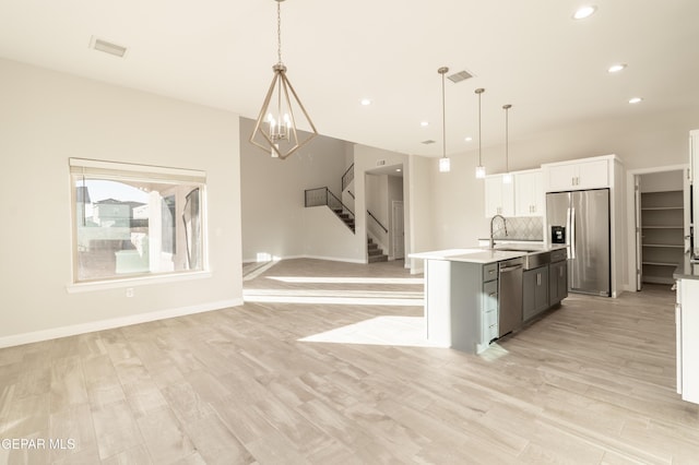 kitchen featuring decorative backsplash, appliances with stainless steel finishes, decorative light fixtures, and a center island with sink