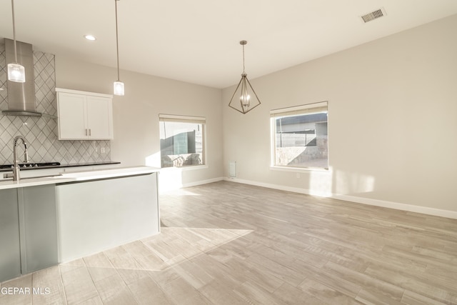 kitchen featuring wall chimney range hood, white cabinetry, and decorative light fixtures