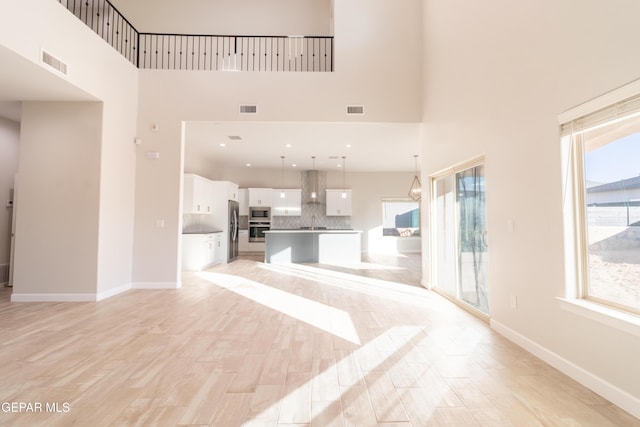 unfurnished living room featuring a healthy amount of sunlight, a towering ceiling, and light hardwood / wood-style flooring