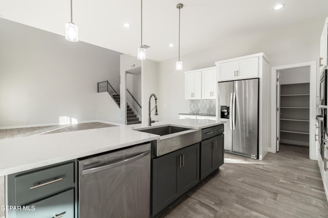 kitchen with appliances with stainless steel finishes, sink, pendant lighting, white cabinets, and hardwood / wood-style floors