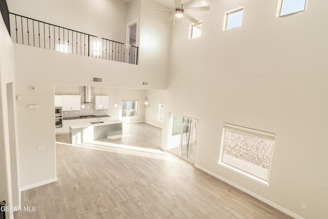 unfurnished living room featuring a towering ceiling, light hardwood / wood-style floors, and ceiling fan