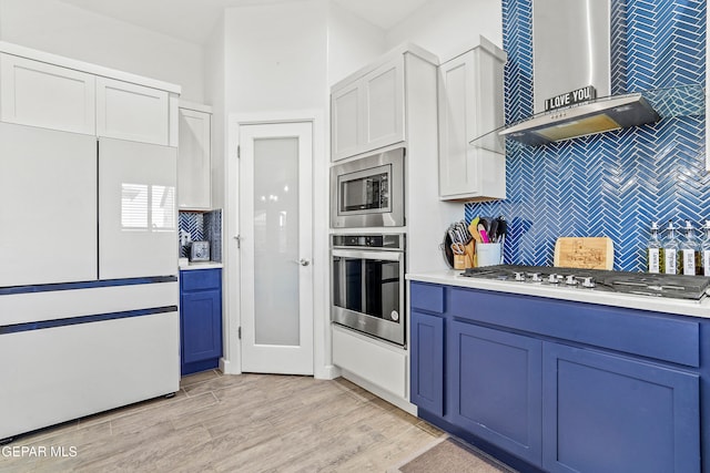 kitchen featuring light wood-type flooring, stainless steel appliances, wall chimney range hood, and blue cabinets