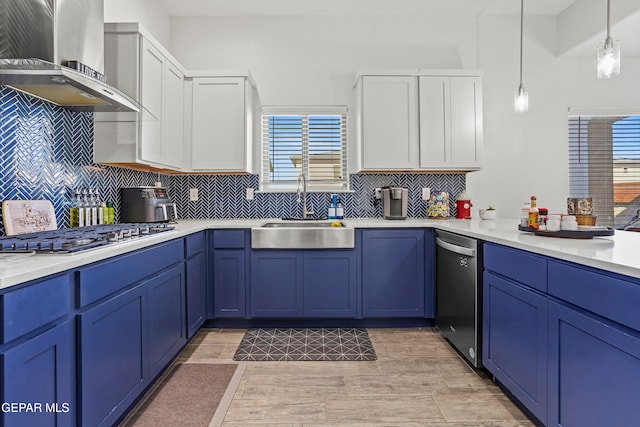 kitchen with white cabinets, wall chimney exhaust hood, blue cabinetry, pendant lighting, and appliances with stainless steel finishes