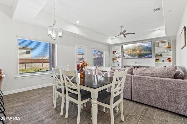 dining area featuring built in features, ceiling fan with notable chandelier, dark hardwood / wood-style flooring, and a tray ceiling