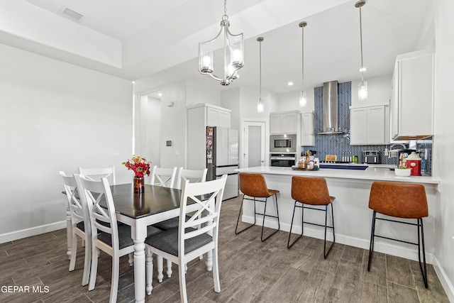 kitchen with stainless steel appliances, white cabinetry, wall chimney range hood, dark hardwood / wood-style floors, and pendant lighting