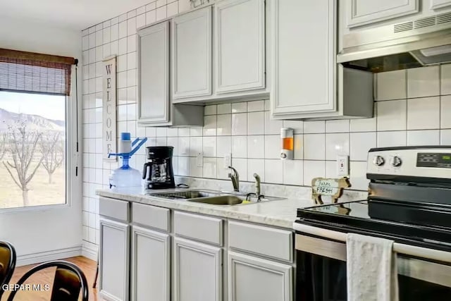 kitchen featuring stainless steel electric range oven, a mountain view, decorative backsplash, light stone counters, and sink