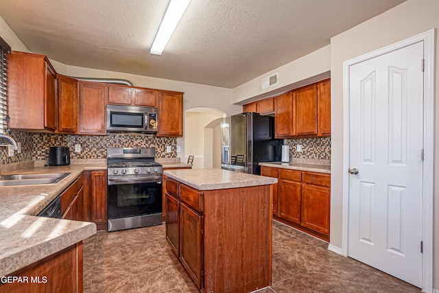 kitchen featuring a textured ceiling, a kitchen island, sink, and appliances with stainless steel finishes