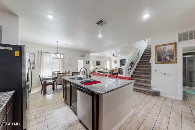 kitchen with light stone countertops, stainless steel appliances, a kitchen island with sink, sink, and pendant lighting