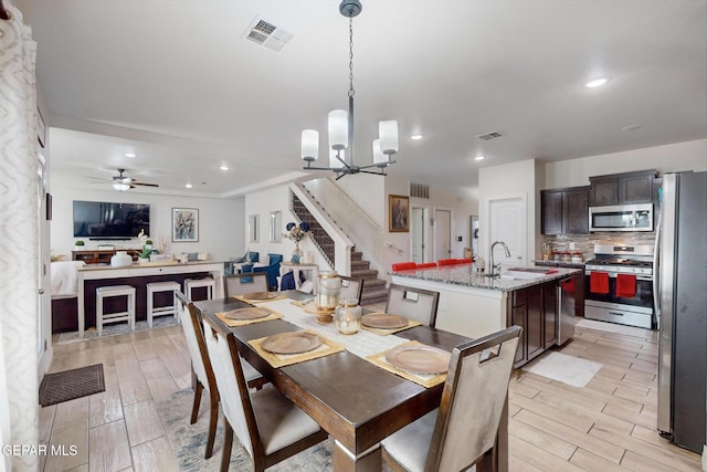 dining room with sink, ceiling fan with notable chandelier, and light wood-type flooring