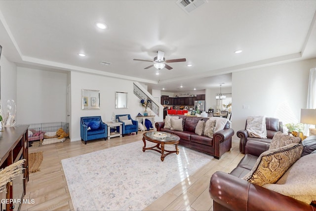 living room with a raised ceiling, light hardwood / wood-style floors, and ceiling fan with notable chandelier