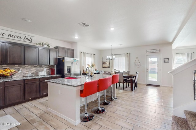 kitchen featuring stainless steel fridge, light stone counters, a breakfast bar, a kitchen island with sink, and pendant lighting