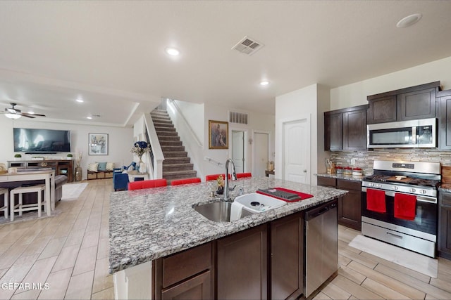 kitchen with sink, an island with sink, light hardwood / wood-style floors, dark brown cabinetry, and stainless steel appliances