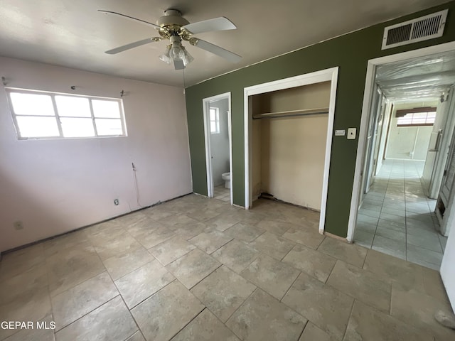 unfurnished bedroom with ensuite bathroom, ceiling fan, a closet, and multiple windows