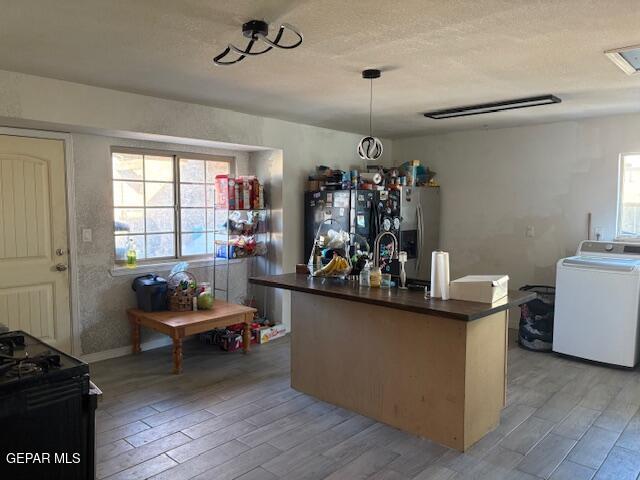 kitchen featuring black appliances, decorative light fixtures, washer / dryer, and light hardwood / wood-style flooring