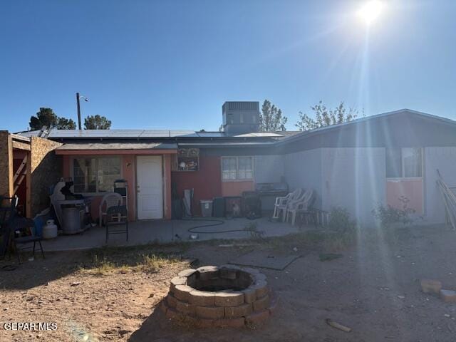 rear view of house with solar panels, a fire pit, central AC unit, and a patio area