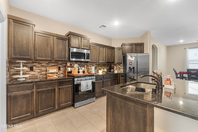 kitchen featuring sink, dark stone countertops, tasteful backsplash, dark brown cabinetry, and stainless steel appliances