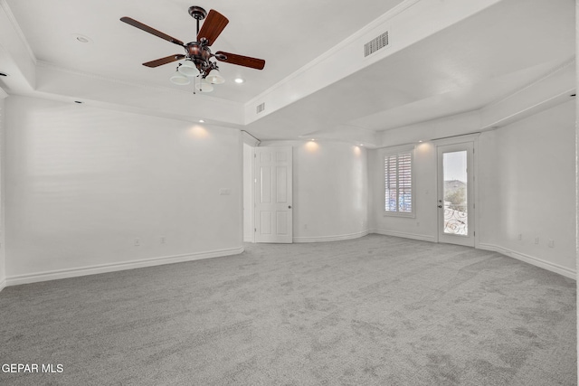 empty room featuring a raised ceiling, ceiling fan, light carpet, and ornamental molding