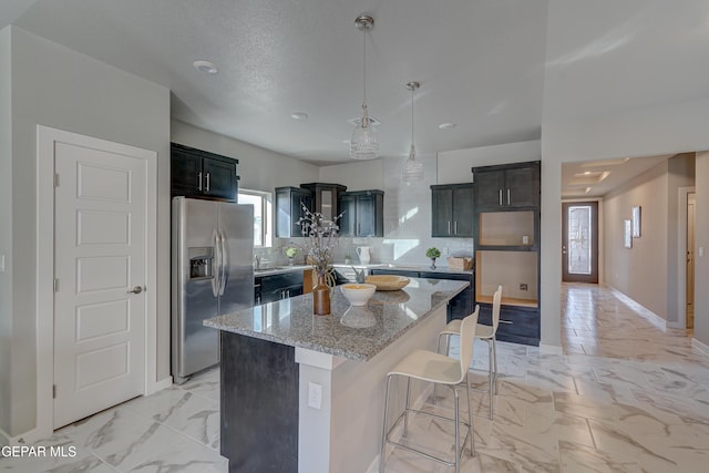 kitchen featuring a kitchen island, marble finish floor, stainless steel fridge with ice dispenser, tasteful backsplash, and a kitchen bar