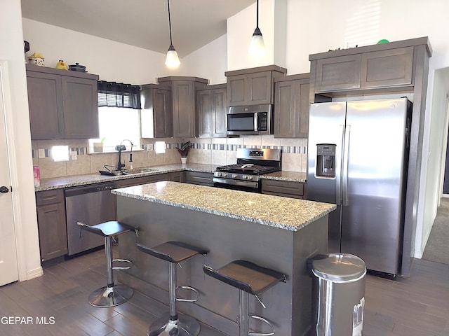 kitchen with a center island, sink, light stone countertops, appliances with stainless steel finishes, and decorative light fixtures