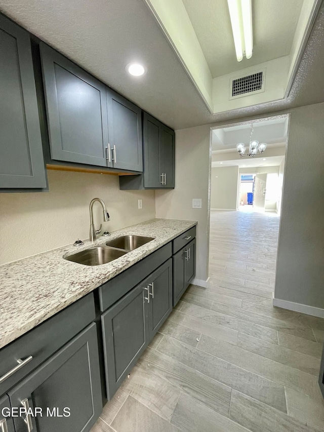 kitchen with light hardwood / wood-style floors, an inviting chandelier, gray cabinetry, and sink