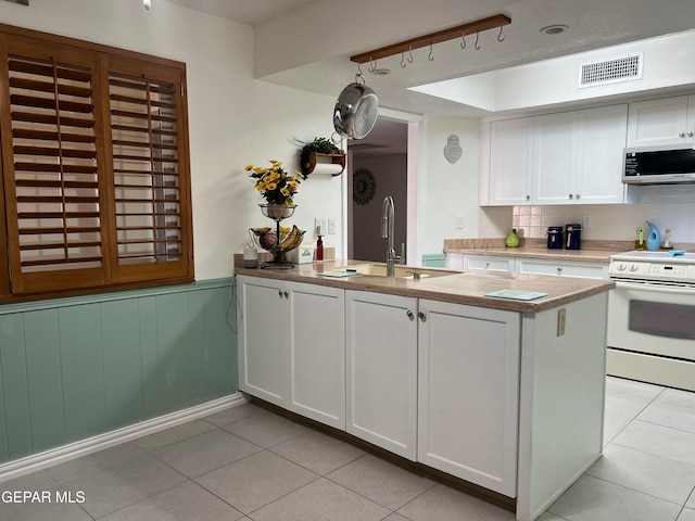 kitchen with sink, light tile patterned floors, kitchen peninsula, white range with electric cooktop, and white cabinets