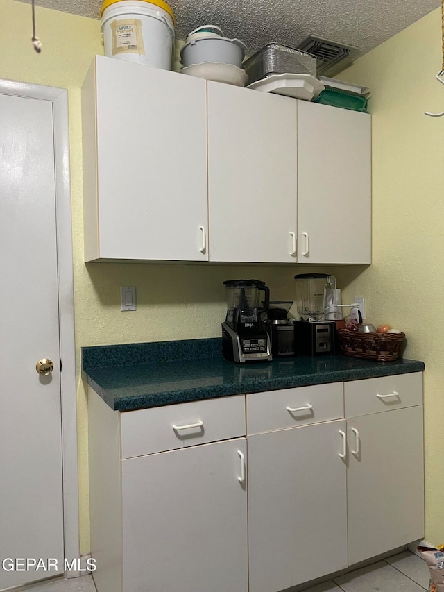 kitchen with a textured ceiling, white cabinets, and light tile patterned flooring