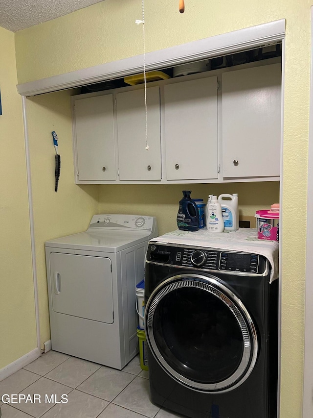 washroom with cabinets, light tile patterned floors, washing machine and clothes dryer, and a textured ceiling