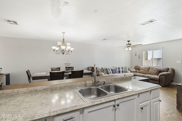 kitchen with pendant lighting, ceiling fan with notable chandelier, sink, light wood-type flooring, and white cabinetry