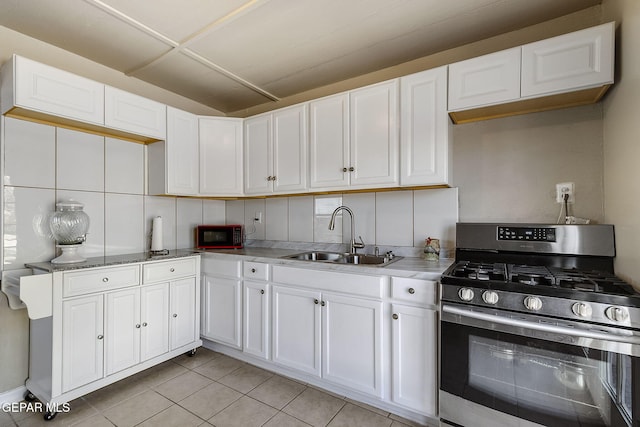 kitchen with white cabinets, stainless steel gas range oven, light tile patterned floors, and sink