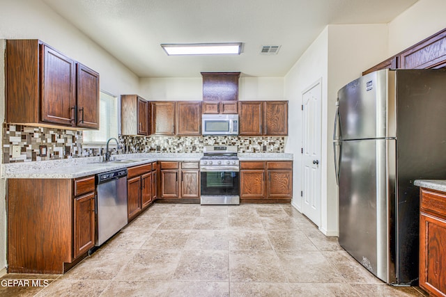 kitchen featuring backsplash, stainless steel appliances, light stone counters, and sink