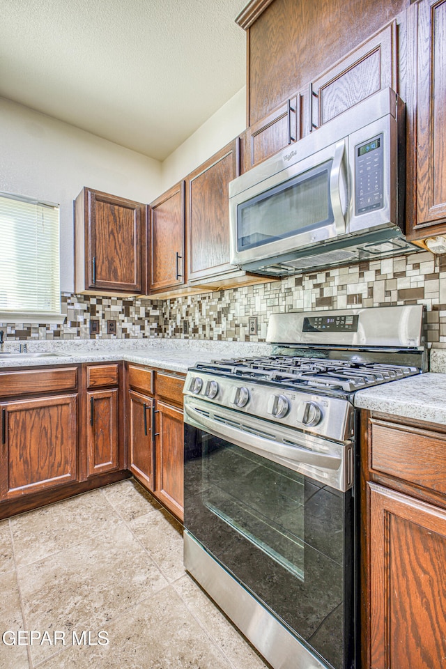 kitchen with backsplash, sink, light tile patterned flooring, and appliances with stainless steel finishes