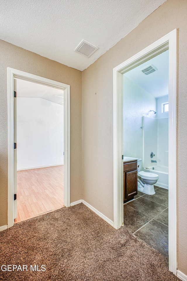 hall featuring dark carpet and a textured ceiling