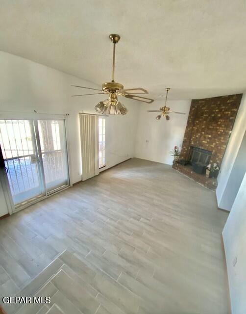 unfurnished living room with a brick fireplace, light hardwood / wood-style flooring, and vaulted ceiling