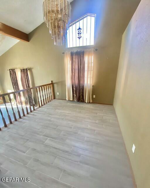 unfurnished room featuring beamed ceiling, a notable chandelier, and high vaulted ceiling