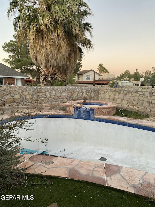 pool at dusk featuring an in ground hot tub