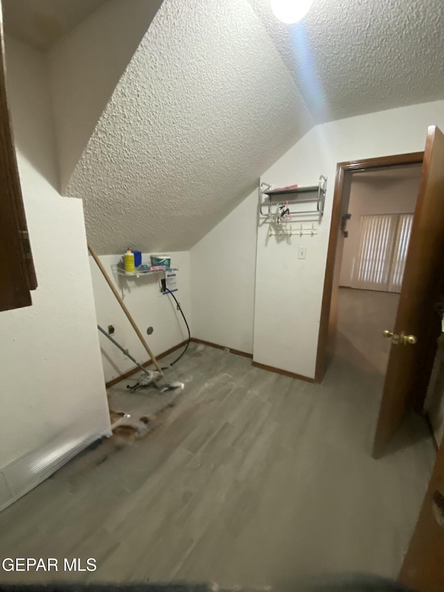 additional living space featuring hardwood / wood-style flooring, vaulted ceiling, and a textured ceiling