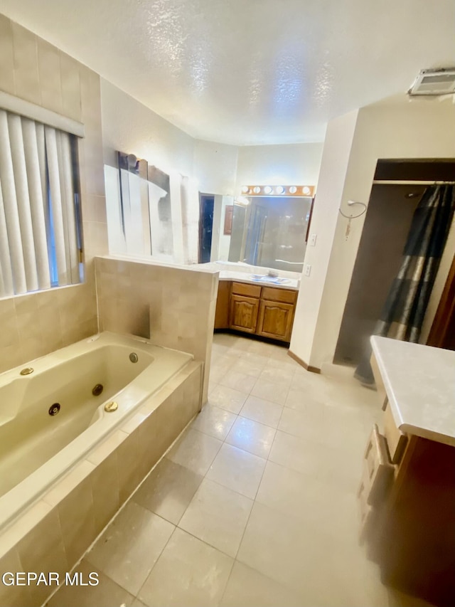 bathroom featuring vanity, tile patterned flooring, a textured ceiling, and tiled tub