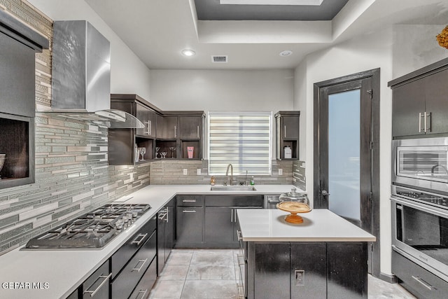 kitchen with sink, wall chimney range hood, decorative backsplash, a kitchen island, and appliances with stainless steel finishes